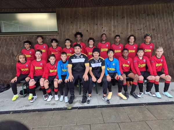 A youth soccer team, consisting of young players and two adults, poses for a group photo outdoors